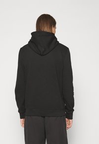 Felpa nera con cappuccio e vestibilità comoda, caratterizzata da polsini e orlo a coste e una texture liscia. Nessun motivo o accento visibile.