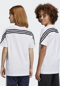 Camisetas de algodón blancas con un diseño de tres rayas negras en la parte de atrás, mangas cortas y cuellos redondeados. Corte casual.