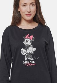 Maglietta nera a maniche lunghe con una grafica di Minnie Mouse che indossa un fiocco rosa e la scritta "MINNIE Mouse" in rosa e bianco. Materiale in cotone morbido.