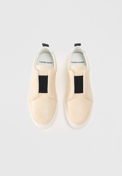 Tenisi slip-on bej din microfibra, cu o bandă elastică neagră pe partea superioară, tălpi din cauciuc alb și branțuri cu marcă.