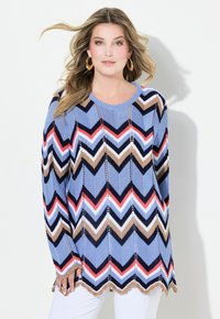 Stickad tunika med ett zigzag-mönster i blått, rött, vitt, brunt och svart. Långa ärmar och scallopad nederkant; texturerat stickat material.