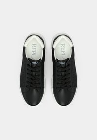 Une paire de baskets basses noires avec des lacets noirs, des semelles blanches et des semelles intérieures marquées "REPLAY", vues de dessus sur un fond blanc.