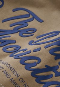 Tessuto beige con lettere blu in rilievo che mostrano "L'Associazione di...". Texture liscia con caratteristiche di design chiare e audaci.