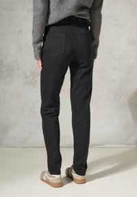Vaqueros skinny negros de mezcla de algodón, con dos bolsillos traseros y una textura suave. Combinados con zapatillas beige y un suéter gris.