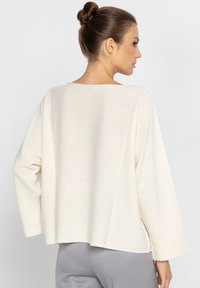 Kremowy sweter dzianinowy o luźnym kroju, z szerokimi rękawami i dekoltem łódkowym, z teksturowanym wzorem na miękkiej, lekkiej tkaninie.