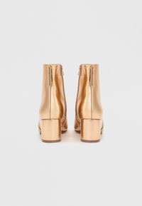 Botines metálicos dorados con textura suave, tacones cuadrados y cremalleras traseras. Diseño limpio con acentos mínimos.