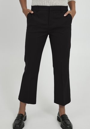 Black cropped trousers with a smooth texture, side pockets, and a fitted waistband. Paired with glossy black loafers.