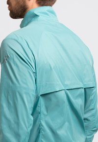 Lichtgewicht turquoise jack met een hoge kraag en een rugventilatie-detail. Gemaakt van een gladde, waterafstotende stof met een getailleerd ontwerp.
