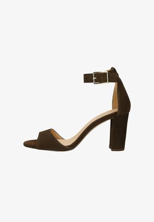 Brązowy zamszowy sandał na wysokim obcasie z odkrytymi palcami, paskiem na kostkę i srebrną klamrą, obcas typu blok zapewniający stabilność.