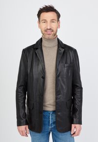 Czarna skórzana marynarka z dwoma przednimi kieszeniami i pojedynczym zapięciem na guzik, noszona na beżowym swetrze z golfem, w komplecie z niebieskimi dżinsami.