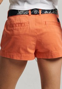 Pomarańczowe bawełniane szorty z listwą w czarny wzór paisley. Posiadają dwie tylne kieszenie i prosty krój na dole.