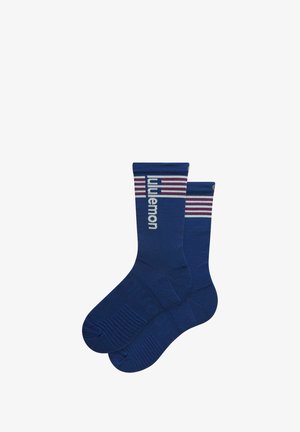 Pár modrých ponožek posádkového střihu s žebrovanou strukturou, na kterých je nápis "lululemon" a červené a bílé pruhy u horní manžety.