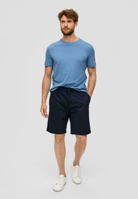 Hellblaues Baumwoll-T-Shirt mit rundem Ausschnitt, kombiniert mit dunkelblauen Shorts mit Kordelzug. Abgerundet mit weißen Sneakers und einem minimalistischen Design.