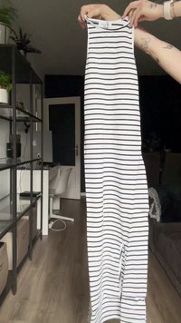 Randig ärmlös klänning med vertikala svarta ränder på vit bakgrund, som visar en rak design och en lång silhuett.