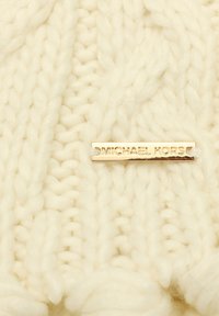 Tessuto lavorato a maglia di colore crema, con filo spesso e texture. Placchetta in metallo color oro con la scritta "MICHAEL KORS" ben in evidenza.