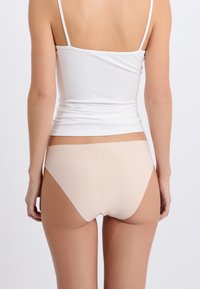 Nude, gładka bielizna bezszwowa, wysokie wycięcie i gładki materiał, o minimalistycznym designie, połączona z białym obcisłym topem na ramiączkach.