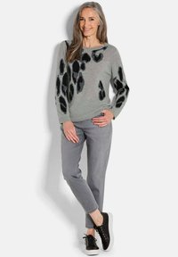 Maglione grigio chiaro con stampa animale nera, abbinato a pantaloni grigi e sneakers nere. Texture morbida, design casual.