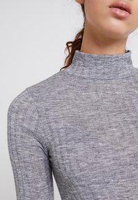 Grau gestreifte Rollkragenbluse mit langen Ärmeln, aus strukturiertem Stoff und figurbetontem Schnitt, der ein schickes Stehkragen-Detail hervorhebt.