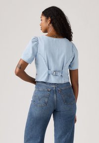 Lichtblauwe denim cropped shirt met korte pofmouwen en een gespsluiting aan de achterkant, gecombineerd met high-waisted blauwe jeans.