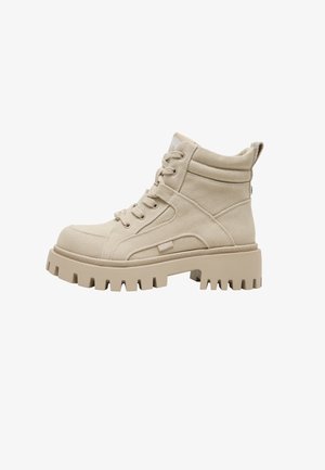 Beige hoge canvaslaars met dikke, grove zool, veterluiting, gewatteerde enkelkraag en lus aan de hiel voor gemakkelijk aantrekken.