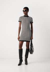 Aansluitende zwart-witte DKNY logo jurk met korte mouwen, gecombineerd met kniehoogte zwarte laarzen en een gebonden zwarte handtas.
