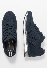 Navyblaue Sportschuhe mit einem gestrickten Obermaterial, strukturierten Einsätzen und einem glänzenden silbernen Akzent an der Ferse. Verfügt über eine flache, gerillte Sohle.