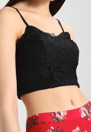 Woman wearing a black lace crop top with thin straps and high-waisted red pants with a floral pattern.