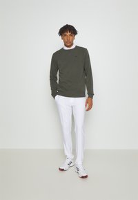 Grønn genser med rund hals, hvit skjorte under, kombinert med hvite bukser og hvite joggesko. Enkel, avslappet design.
