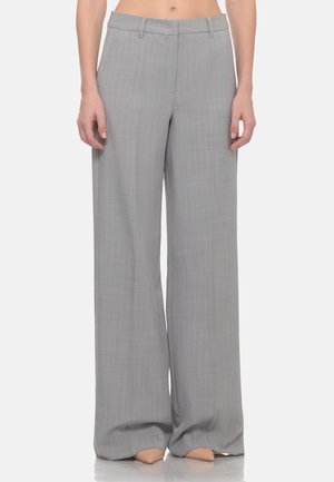 Pantaloni grigi a gamba larga con un delicato motivo a quadri indossati da una persona in piedi, abbinati a scarpe beige con punta affusolata.