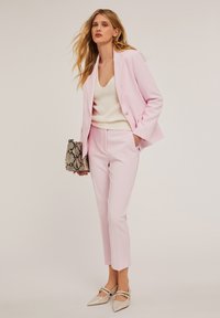 Lichtroze op maat gemaakte pak met een enkel-knoop blazer en slim-fit broeken. Gecombineerd met een witte gebreide top en een handtas met slangprint. Beige schoenen.