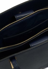 Wnętrze granatowej skórzanej torebki z złotymi detalami zamka błyskawicznego, zawierającej wiele compartmentów i gładką teksturę. Nie pokazano widoku zewnętrznego.