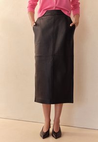 Czarna skórzana spódnica midi z bocznymi kieszeniami, z przeszywanymi panelami, gładką fakturą i prostym krojem. Noszona z czarnymi butami o zaostrzonym nosku.