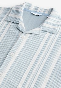 Chemise à col court à manches courtes, présentant un tissu texturé avec des rayures verticales bleues et blanches, cinq boutons et un col doux.