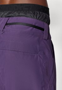 Pantalones cortos morados de exterior con una textura suave, que presentan una cinturilla negra y un detalle de bolsillo. Marca ClimaProof en el lado.