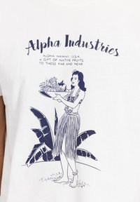 Tricou alb din bumbac, cu un grafic bleu închis ce reprezintă o femeie ținând o tavă cu fructe, înconjurată de frunze tropicale și cu textul "Alpha Industries" deasupra.