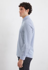 Light blue and white striped button-up shirt, long sleeves, cotton fabric, classic collar, single button on each cuff, tailored fit.