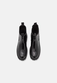Botas Chelsea de charol negro con un acabado brillante, paneles elásticos en los laterales y tiradores, con una suela de goma texturizada para mayor agarre.