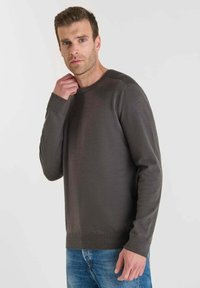 Mörkgrå stickad tröja med rund hals, ribbade mudd och strukturerad axeldetalj. Matchad med ljusblå jeans.