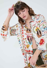 Colorful, patterned blouse with long flared sleeves. Features floral motifs, illustrations, and embroidered accents on a light fabric.