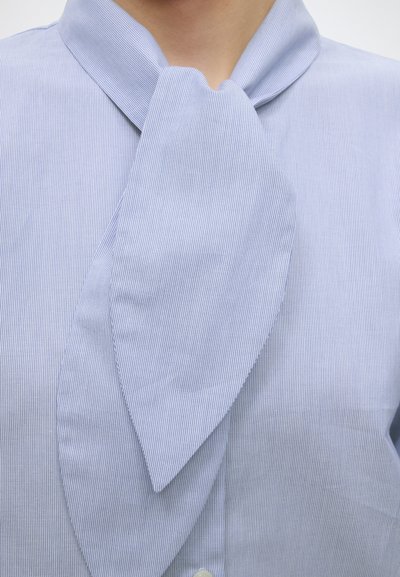 Gros plan d'une personne portant une chemise bleu clair avec un grand nœud joliment noué au col.