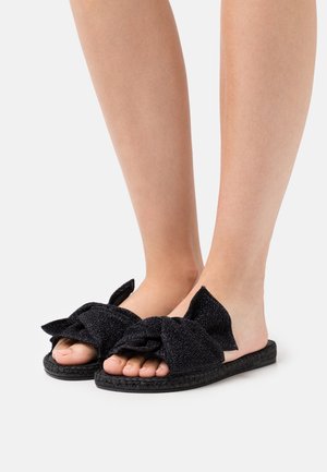 Zwarte slide-sandalen met een textiel bovenwerk en een grote strikdetail, een platte geweven zool en een open teenontwerp.