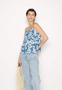 Top de alças com estampa floral em azul, apresentando flores brancas, alças finas ajustáveis e um corte solto. Combinado com calças largas em azul claro.