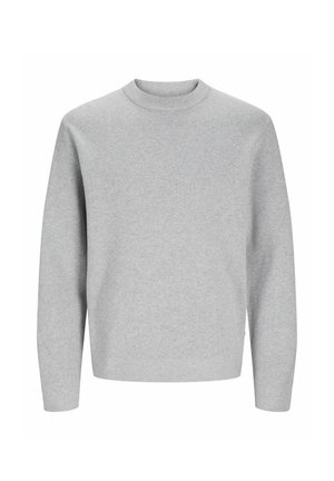 Dziecko ubrane w jasno-szary sweter z długim rękawem, ciemnoszare luźne spodnie i białe trampki stojące na jednolitym tle.