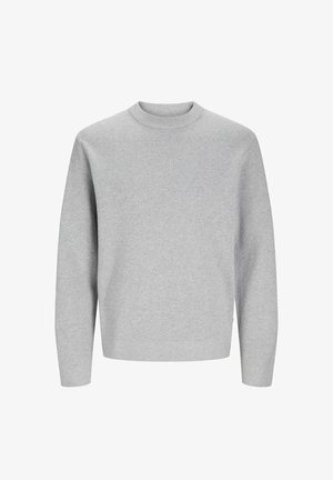 Dziecko ubrane w jasno-szary sweter z długim rękawem, ciemnoszare luźne spodnie i białe trampki stojące na jednolitym tle.