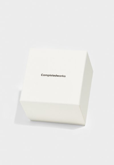 Λευκό τετράγωνο κουτί με λεία υφή, που διαθέτει το κείμενο "Completedworks" εκτυπωμένο σε μινιμαλιστική, σκούρα γραφή στην πάνω επιφάνεια.
