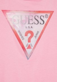 Pink t-shirt featuring a large triangular logo in red and white, with "GUESS," "U.S.A.," and the word "WASHED," accented by a question mark inside.