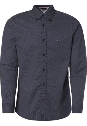 Chemise bleu marine à manches longues avec petit motif à pois blancs et petit logo sur la poche poitrine gauche.
