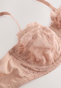 Čipkasti grudnjak u svijetloj boji gola, sadrži složene cvjetne uzorke i delikatne rubove, s mekanim materijalom i podesivim naramenicama za udobno prianjanje.