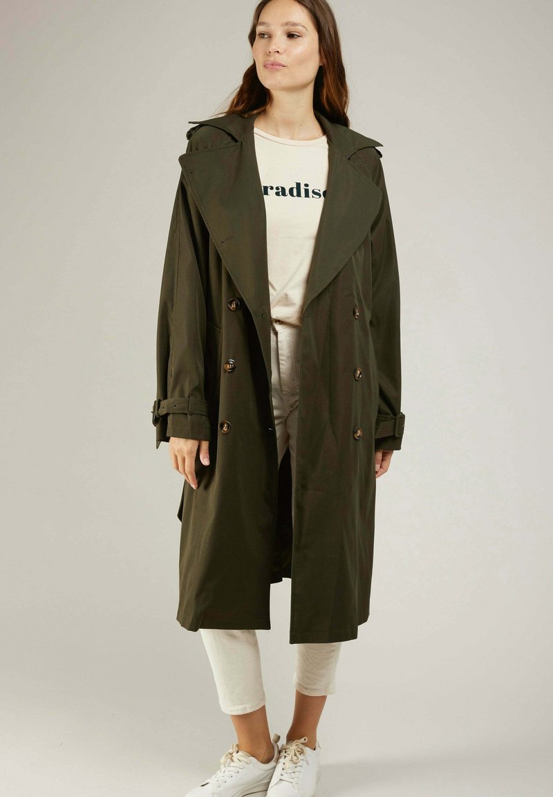 Trench-coat vert olive avec un grand col, un design à double boutonnage et des accents de boutons. Fabriqué à partir d'un tissu lisse et léger.
