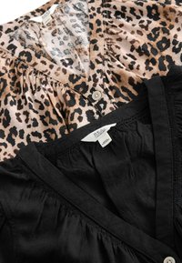 To bluser lagt fladt: en leopardmønstret med knaplukning og rynkede detaljer, den anden helsort med en glat tekstur og elastiske accentuer.